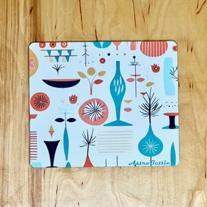May include: A white coaster with a colorful mid-century modern design featuring abstract shapes, geometric patterns, and a teal vase. The coaster has the text "AstroPettie" in the bottom right corner.