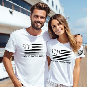 May include: White t-shirts with a black graphic of the American flag and the words "NEVER SURRENDER" printed below. The flag design features a dotted field of stars and horizontal brushstroke stripes.