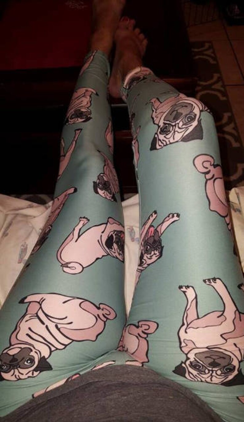 May include: A pair of teal blue leggings with a repeated pattern of pugs in various poses. The pugs are a light pink color with black noses and eyes.