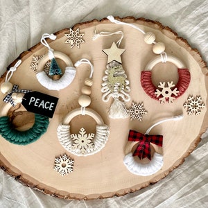 May include: Six handmade wooden Christmas ornaments with different designs. The ornaments are made with natural twine and feature a variety of colors, including green, red, white, and gold. The ornaments are displayed on a wooden slice.