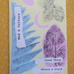 以下が含まれることがあります： 「Mud & Culture」というタイトルと「Issue Three」と「Obtain a yield」というテキストが書かれた薄い黄色の冊子。表紙には青いシダ、ピンクの葉、緑の葉、ピンクの円が描かれている。