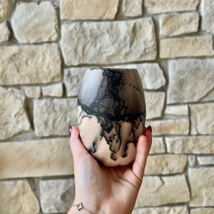 May include: A rounded ceramic vase featuring a smooth, light beige surface adorned with intricate, dark black, web-like patterns that wrap around the exterior. The vessel has a wide, open top and a tapered base, showcasing a distinct smoke-fired finish.