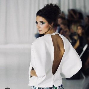 May include: A white top with a low back and a long, flowing cape-like sleeve. The top is paired with a skirt featuring a green and blue scale pattern.