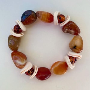 May include: A bracelet made with carnelian stones and white shell beads. The bracelet is brown, orange, and white.