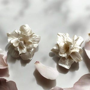 May include: A pair of white flower-shaped earrings with a pearlescent finish. The earrings are made of a soft, pliable material and have a delicate, feminine look.