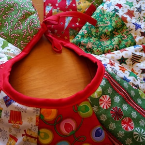 K&ouml;nnte beinhalten: Ein festlicher Weihnachtsbaumrock mit rotem Rand und einer Vielzahl von Stoffflicken mit Feiertagsmotiven. Die Flicken zeigen Zuckerstangen, Sterne, Geschenke und Lichterketten. Der Rock hat einen Durchmesser von etwa 122 cm.