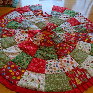K&ouml;nnte beinhalten: Runder Weihnachtsbaumrock mit Patchwork-Design. Der Rock hat rote, gr&uuml;ne und wei&szlig;e Stoffe mit festlichen Mustern wie Sternen, Geschenken und Zuckerstangen. Ein roter R&uuml;schenrand rahmt den Rock ein, und er hat einen Kordelverschluss.