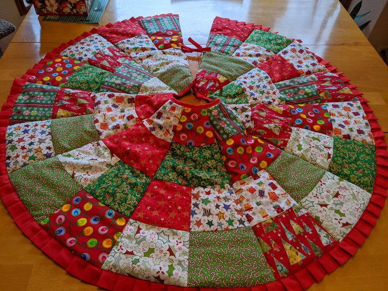 K&ouml;nnte beinhalten: Runder Weihnachtsbaumrock mit Patchwork-Design. Der Rock hat rote, gr&uuml;ne und wei&szlig;e Stoffe mit festlichen Mustern wie Sternen, Geschenken und Zuckerstangen. Ein roter R&uuml;schenrand rahmt den Rock ein, und er hat einen Kordelverschluss.
