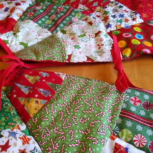 K&ouml;nnte beinhalten: Ein festlicher Weihnachtsbaumrock mit Patchwork-Design. Der Rock zeigt verschiedene Stoffe mit Feiertagsmotiven, darunter Zuckerstangen, Weihnachtsb&auml;ume und Sterne, in Rot, Gr&uuml;n und Wei&szlig;. Ein rotes Band ist zu einer Schleife gebunden.