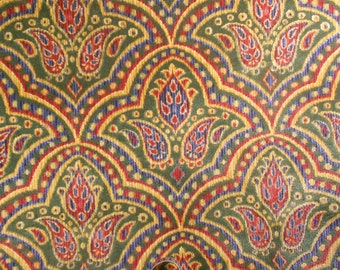May include: A close-up of a green, red, blue, and gold paisley patterned fabric. The fabric has a textured, woven look.