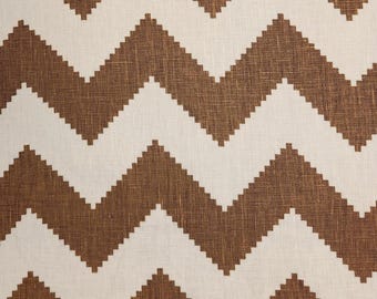 May include: Close-up of a fabric with a repeating zigzag pattern. The pattern features alternating bands of brown and off-white. The fabric has a textured appearance, suggesting a woven material. The design is symmetrical and creates a bold visual effect.