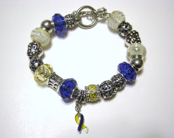 May include: A silver charm bracelet with blue, yellow, and white beads. The bracelet has a silver clasp and a blue and yellow ribbon charm.