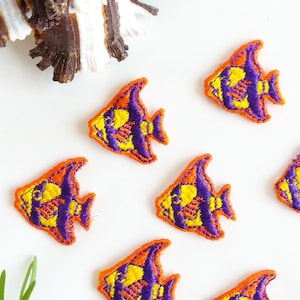 May include: Seven embroidered iron-on patches of colorful fish with orange, yellow, and purple details. The fish are in a variety of positions and are all facing the same direction.