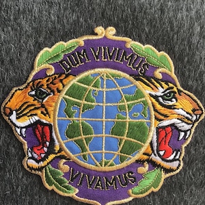 May include: Purple and gold embroidered patch with two tiger heads flanking a globe. The text "Dum Vivimus Vivamus" is written around the globe.
