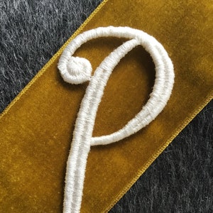 May include: White embroidered letter P on a gold velvet ribbon.