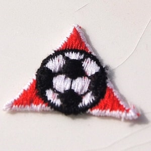 May include: A red triangle-shaped patch with a white and black soccer ball design in the center.