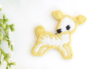 以下が含まれることがあります： 漫画の鹿の刺繍が施された黄色のアイロン接着パッチが2つ。鹿は白で、目は黒く、鼻は黒いです。
