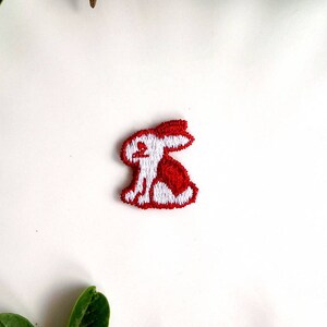May include: White embroidered bunny rabbit patch with red accents. The patch is on a white background.