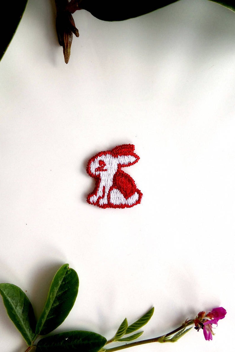 May include: White embroidered bunny rabbit patch with red accents. The patch is on a white background.