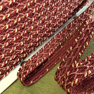 May include: Red and gold braided trim with a diamond pattern. The trim is made of a soft, textured fabric.
