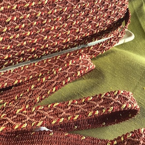May include: Red, gold, and brown braided trim with a woven pattern. The trim has a decorative edge.
