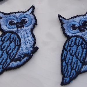 May include: Two blue embroidered owl patches with black stitching. The owls have a light blue body and dark blue wings.