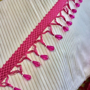 May include: Pink and white trim with a beaded fringe. The trim is made of a crocheted fabric with small pink beads hanging from it.