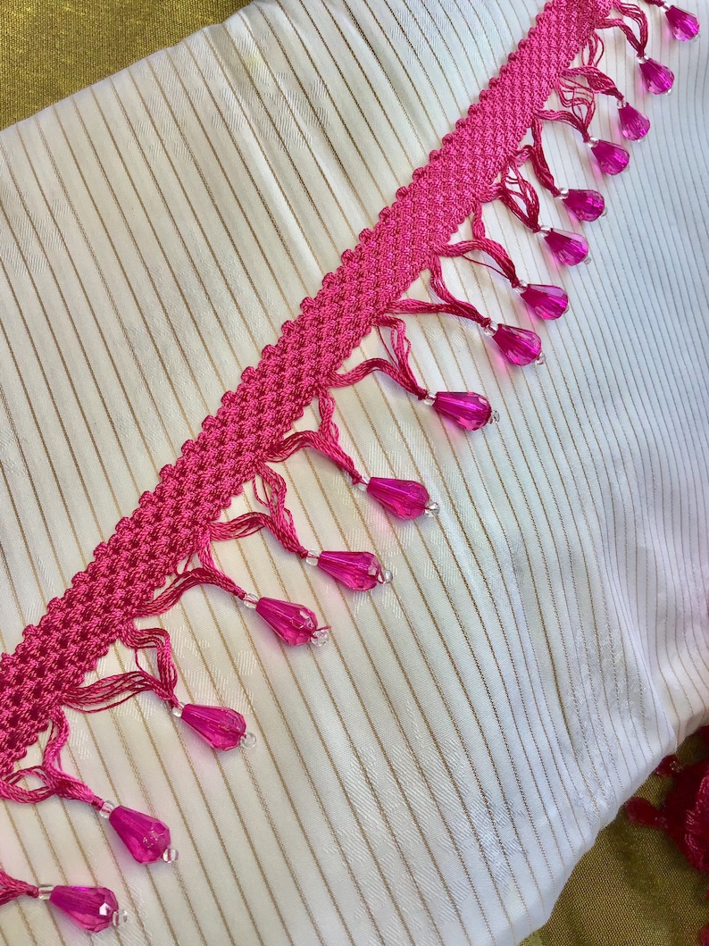 May include: Pink and white trim with a beaded fringe. The trim is made of a crocheted fabric with small pink beads hanging from it.