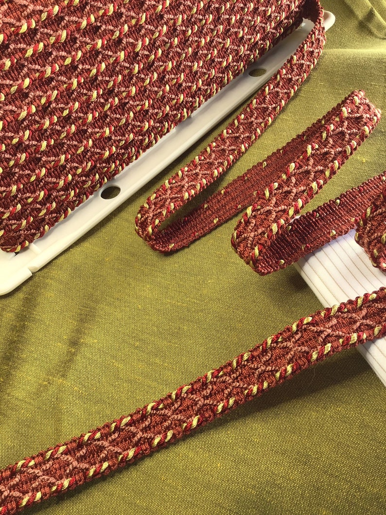 May include: Red and gold braided trim with a diamond pattern. The trim is woven with a textured, rope-like cord.