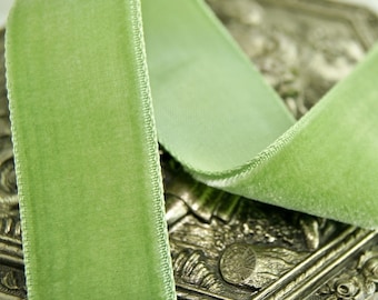 May include: A close-up of a light green velvet ribbon with a satin edge. The ribbon is folded and draped over a silver-colored surface.
