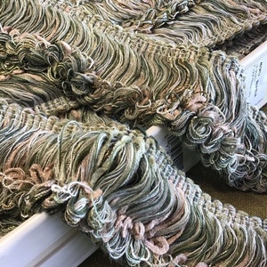 May include: Green, pink, and gold fringe trim with a wavy texture. The trim is made of multiple strands of yarn and has a delicate, feminine look.