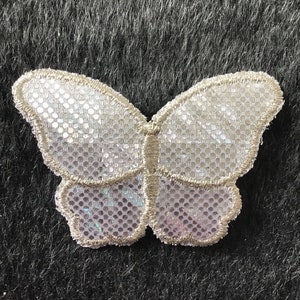 Pode incluir: Uma aplicação de borboleta prateada brilhante com um centro de malha branca. A borboleta é contornada com fio prateado.