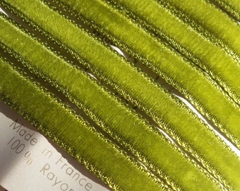 May include: Close-up of a roll of olive green velvet ribbon with gold trim. The ribbon is made of 100% rayon and is labeled "Made in France". The ribbon is angled across the frame.
