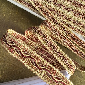 May include: Close-up of gold and burgundy braided trim. The trim has a woven design and is perfect for adding a touch of elegance to any project.