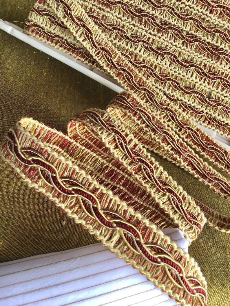May include: Close-up of gold and burgundy braided trim. The trim has a woven design and is perfect for adding a touch of elegance to any project.
