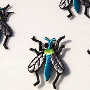 May include: Four embroidered iron-on patches of blue and green flies with black legs and silver wings.