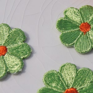 May include: Three green felt flower patches with orange centers. The flowers have five petals each.