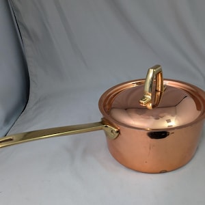 May include: A copper saucepan with a brass handle and lid. The lid has a brass handle. The saucepan is round and has a long handle. The handle has a hole at the end. The pot is approximately 6 inches in diameter.