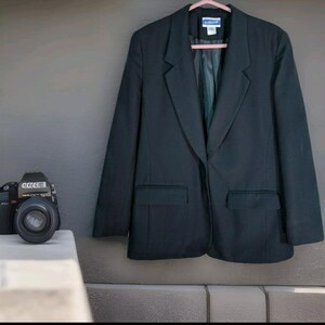 May include: A black blazer with a single button closure and two pockets. The blazer has a classic, tailored fit.