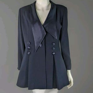 May include: A dark navy blue blazer featuring a deep V-neckline with wide satin lapels. The garment has long sleeves, a tailored fit, and a flared hemline. It is accented with six fabric-covered buttons arranged in two vertical rows of three.
