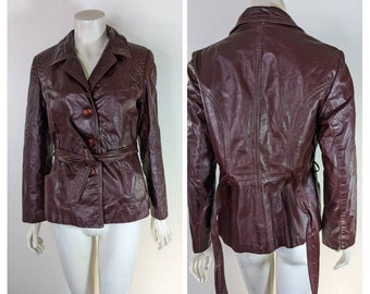 May include: A burgundy leather jacket with a belted waist and a button-up front. The jacket has a classic style and is in good condition.