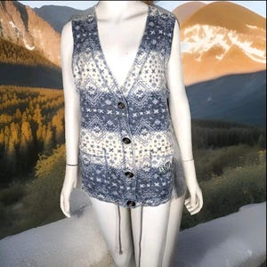 May include: A blue and white patterned knit waistcoat with a V-neck and button fastening. The waistcoat has two pockets and a drawstring at the bottom.