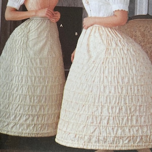 Könnte beinhalten: Zwei weiße Baumwoll-Petticoats, einer mit einem gestreiften Muster und der andere mit einem Blumenmuster. Beide Petticoats sind gerafft und haben eine volle, fließende Form.