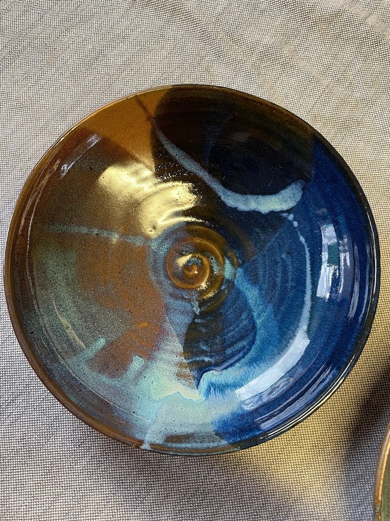May include: A large, round ceramic bowl with a blue, brown, and white glaze. The bowl has a unique, swirling pattern.