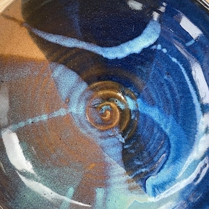 May include: A large ceramic bowl with a blue, brown, and white glaze. The bowl has a swirling pattern and a glossy finish.