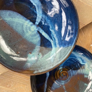May include: Two ceramic plates with a blue and brown glaze. The plates have a swirling pattern and a glossy finish.