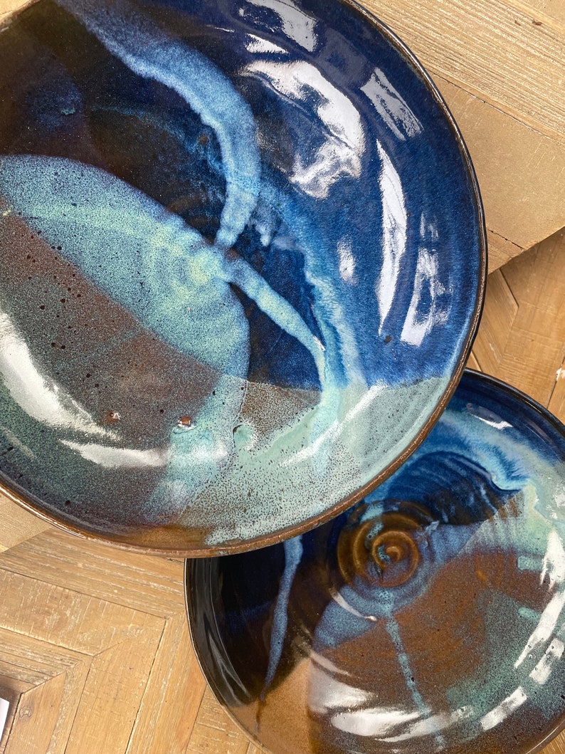May include: Two ceramic plates with a blue and brown glaze. The plates have a swirling pattern and a glossy finish.