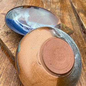 May include: Two ceramic plates, one with a blue and brown glaze and the other with a brown and white glaze. The plates are on a wooden surface.