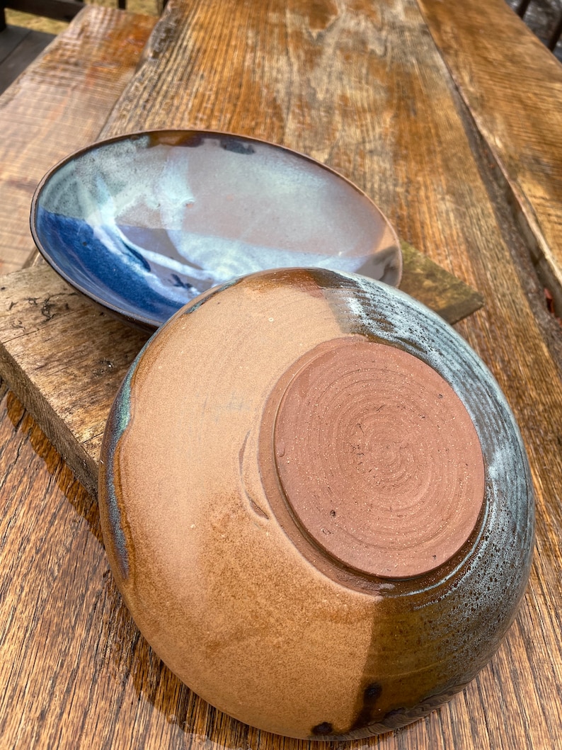 May include: Two ceramic plates, one with a blue and brown glaze and the other with a brown and white glaze. The plates are on a wooden surface.