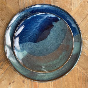 May include: A set of two ceramic plates in shades of blue, green, and brown. The plates are glazed and have a rustic, handmade look.